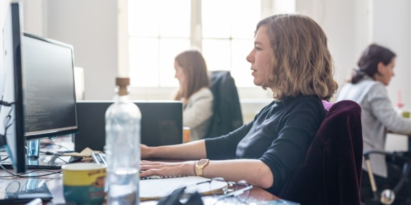 Kvinne som ser på en pc skjerm i et kontorlandskap.