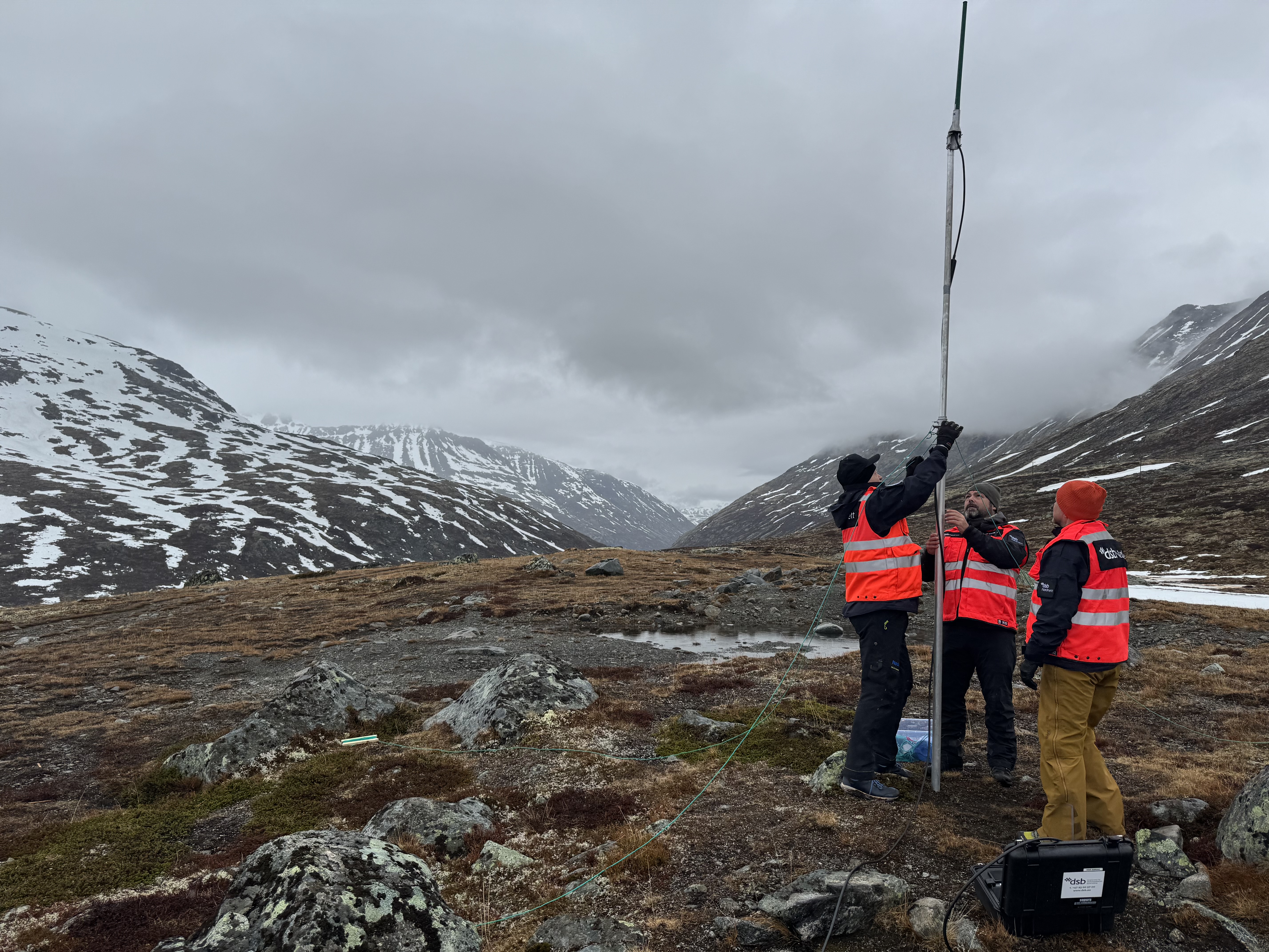Tre medarbeidere fra DSB setter opp antenne i fjellandskap.