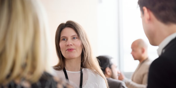 Kvinne med langt hår og hvit genser som står og ser på en mann og en kvinne