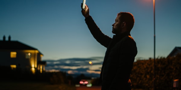 En person holder en mobil opp i luften, i et forsøk på å få mobildekning.
