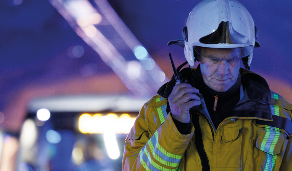 Forsidebilde fra rapporten Nødnett i bruk. På bildet er det en brannmann som snakker i en radioterminal.