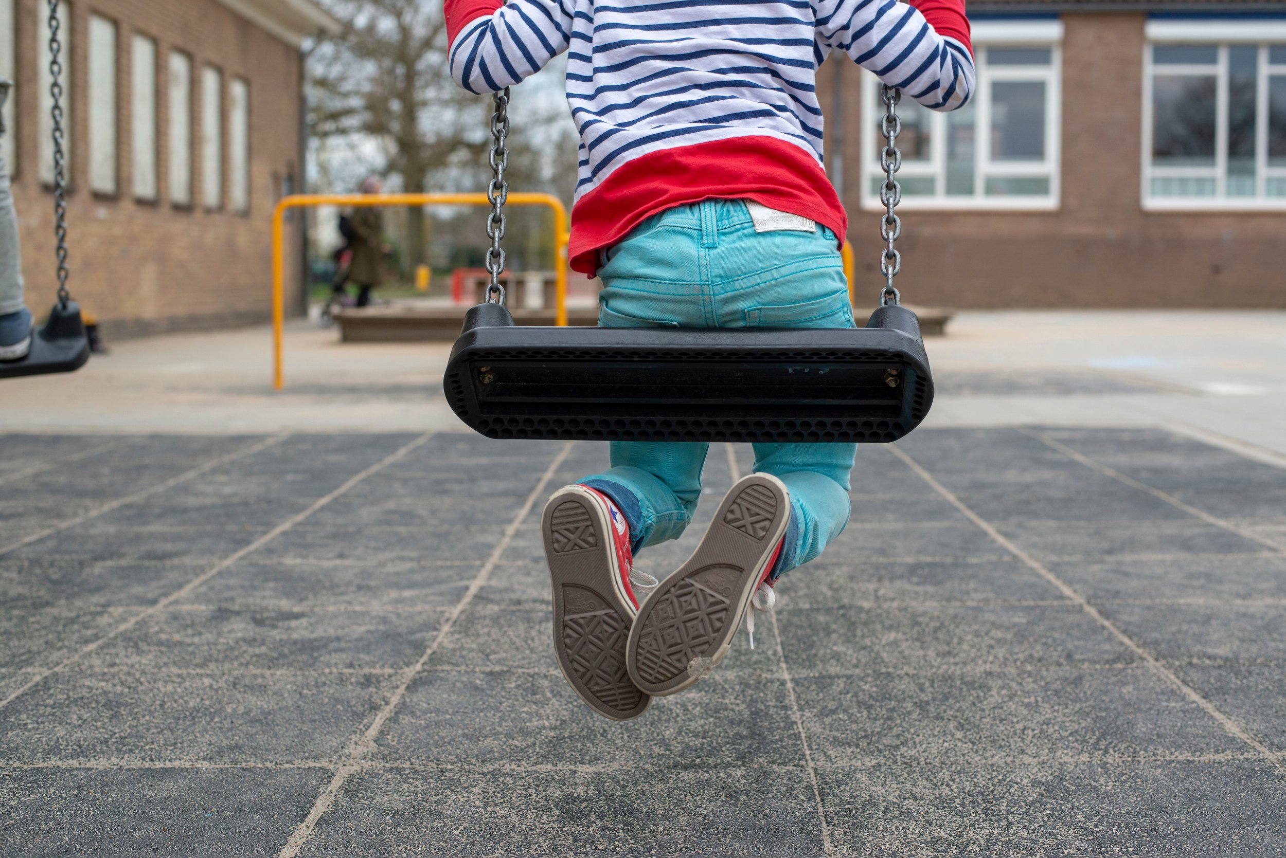 Barn som sitter på en huske i på en lekeplass.