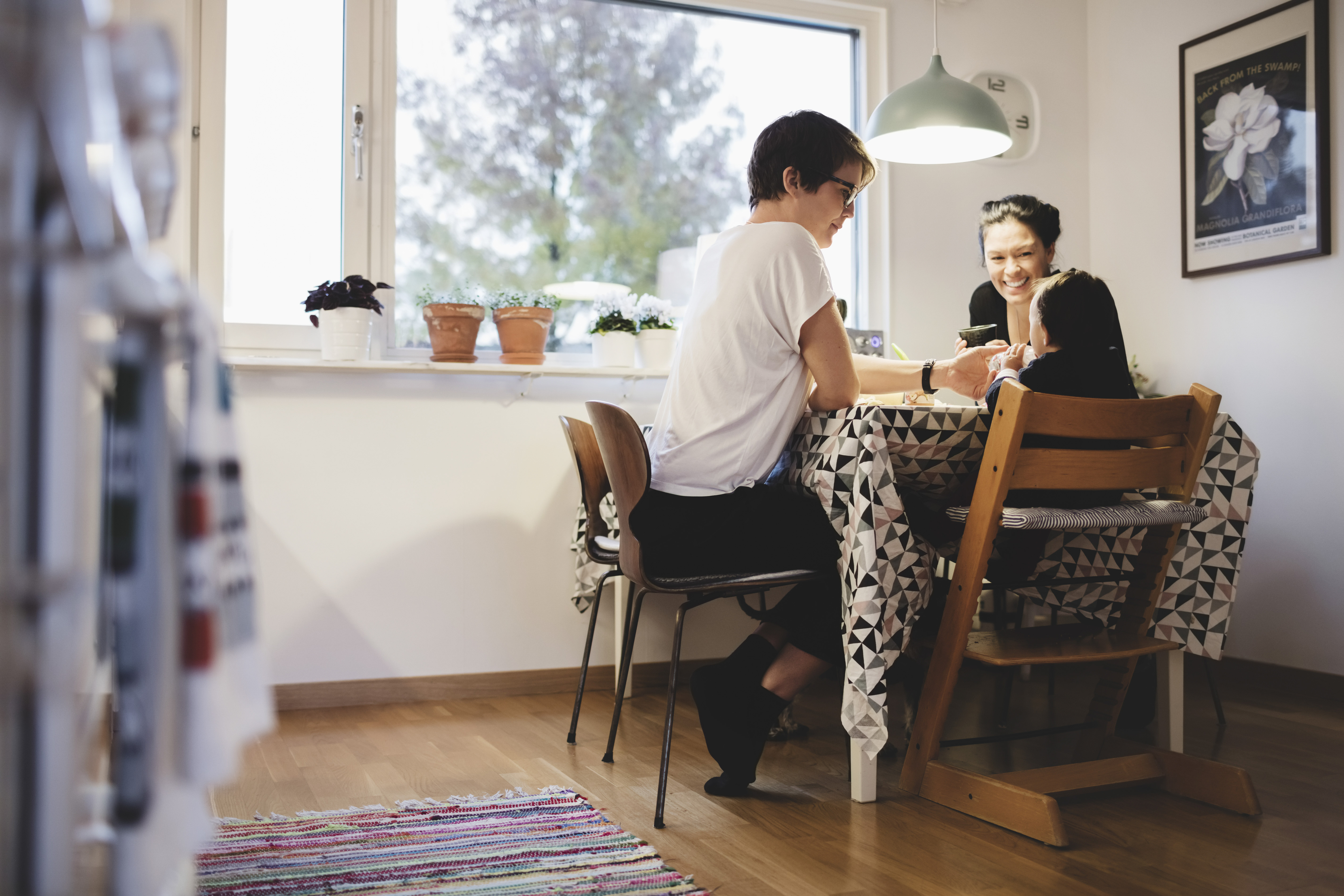 Two women and a small child at a kitchen table. One of the women smiles at the child.