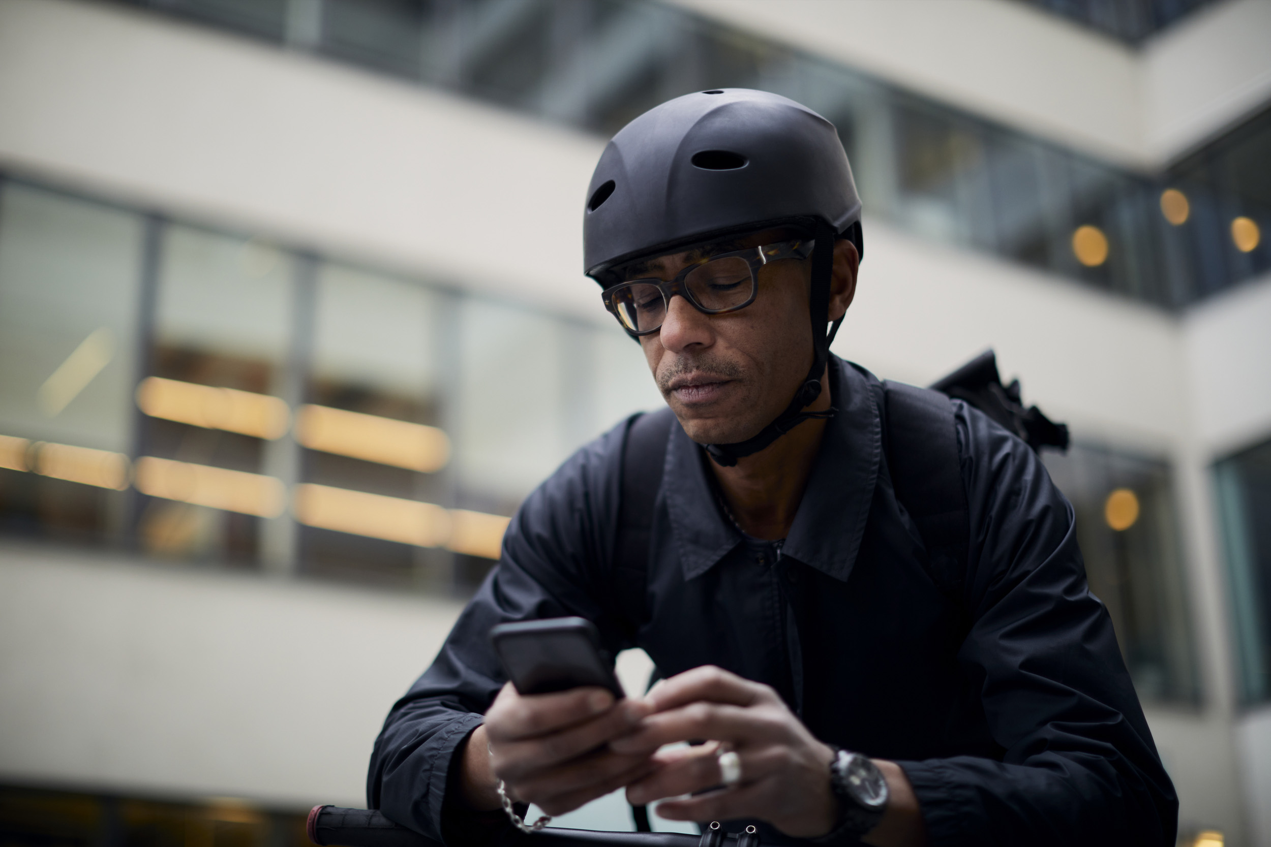 Mann med sykkelhjelm bruker smarttelefon utenfor kontorbygning
