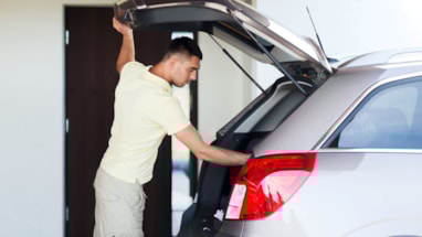 Mann som legger noe i bagasjerommet på en sølvgrå personbil