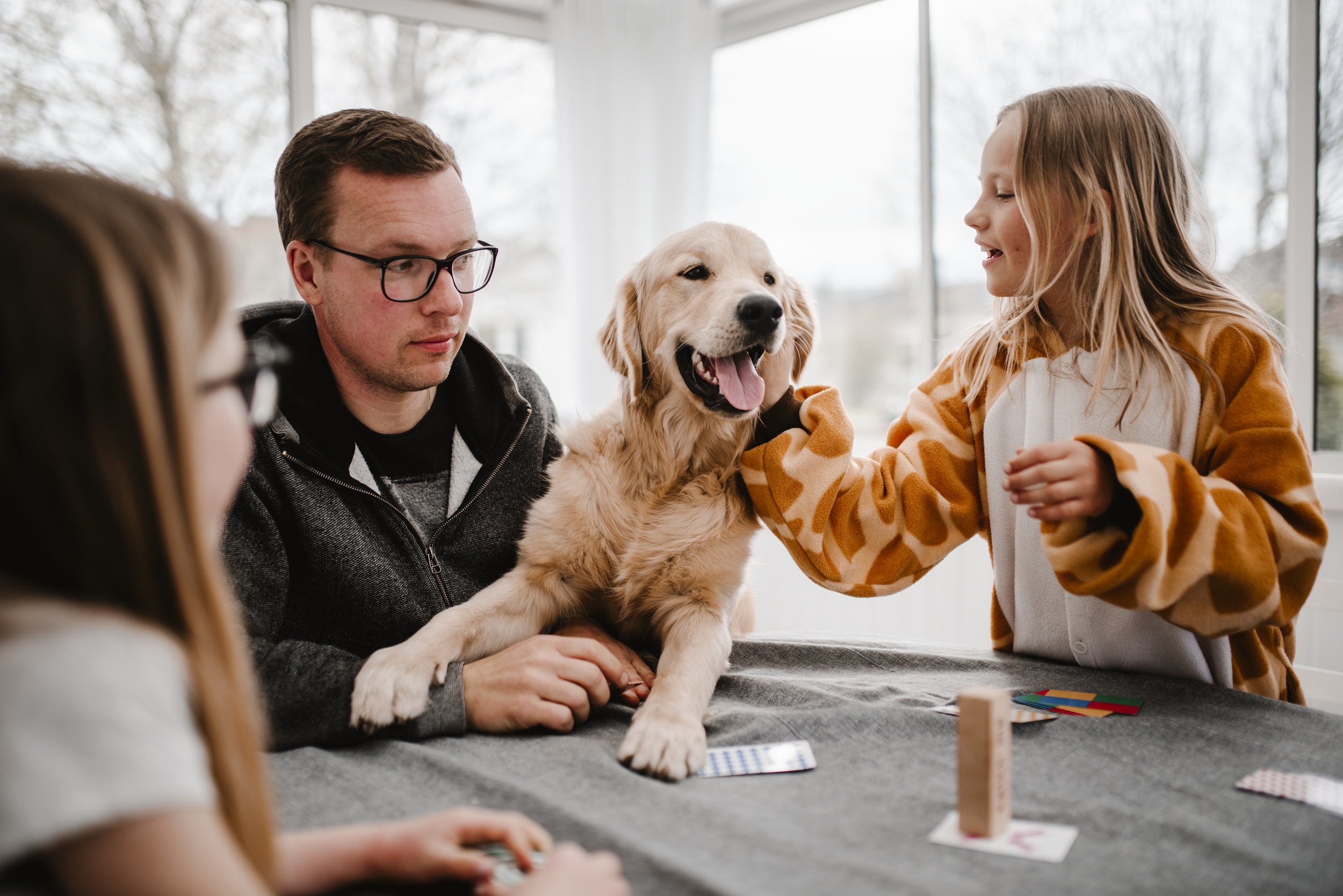 En glad familiehund står mellom en voksen og et barn. 