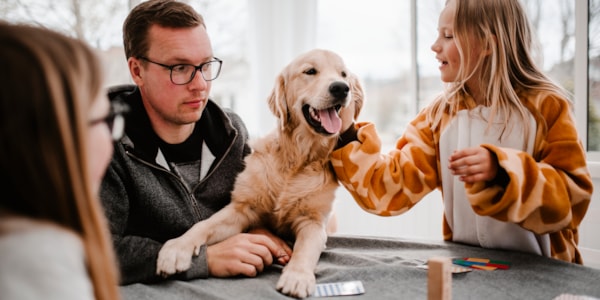 En glad familiehund står mellom en voksen og et barn.