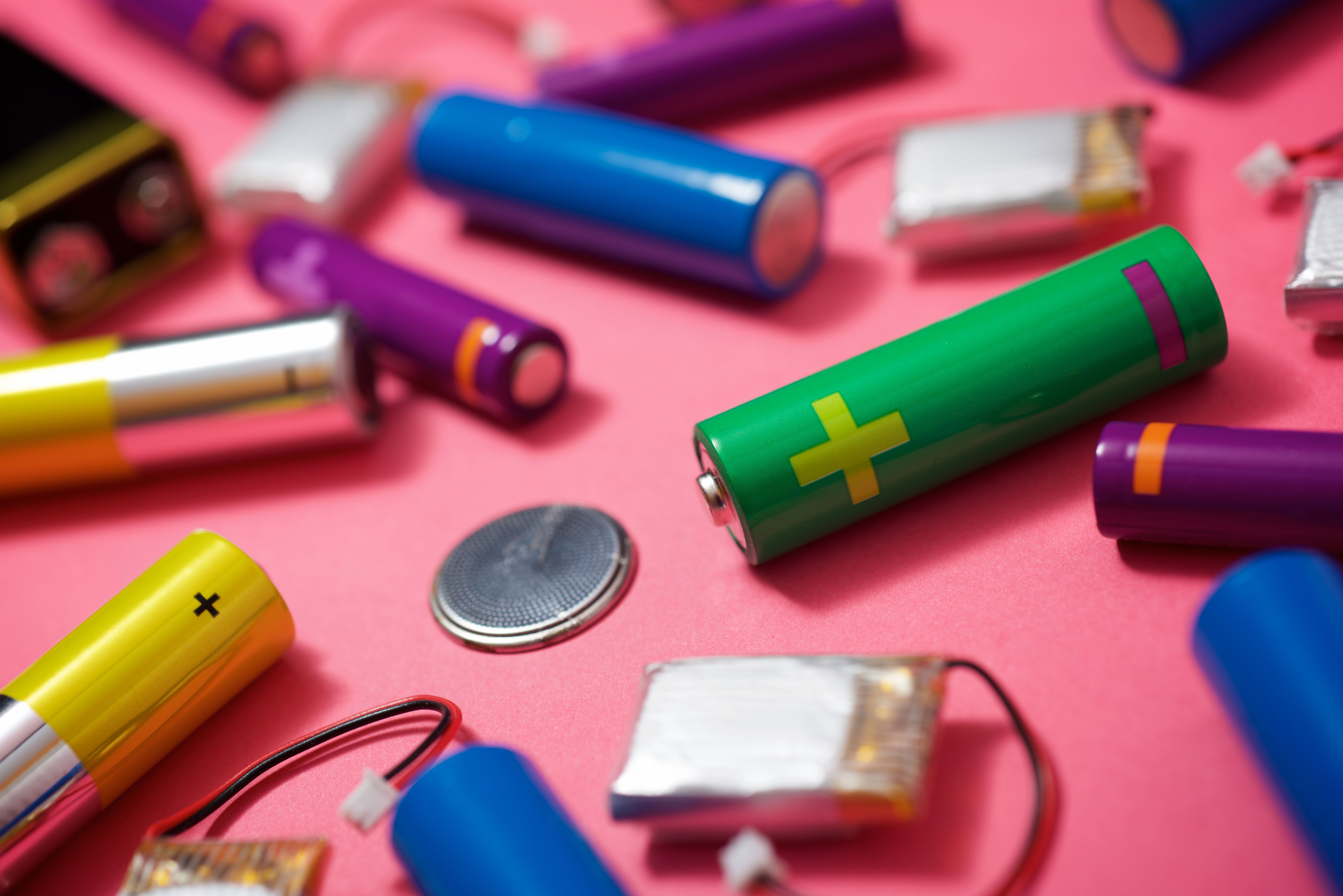 Ulike typer batterier på rosa bakgrunn, inkludert AA-batterier, knappcellebatteri og oppladbare batterier