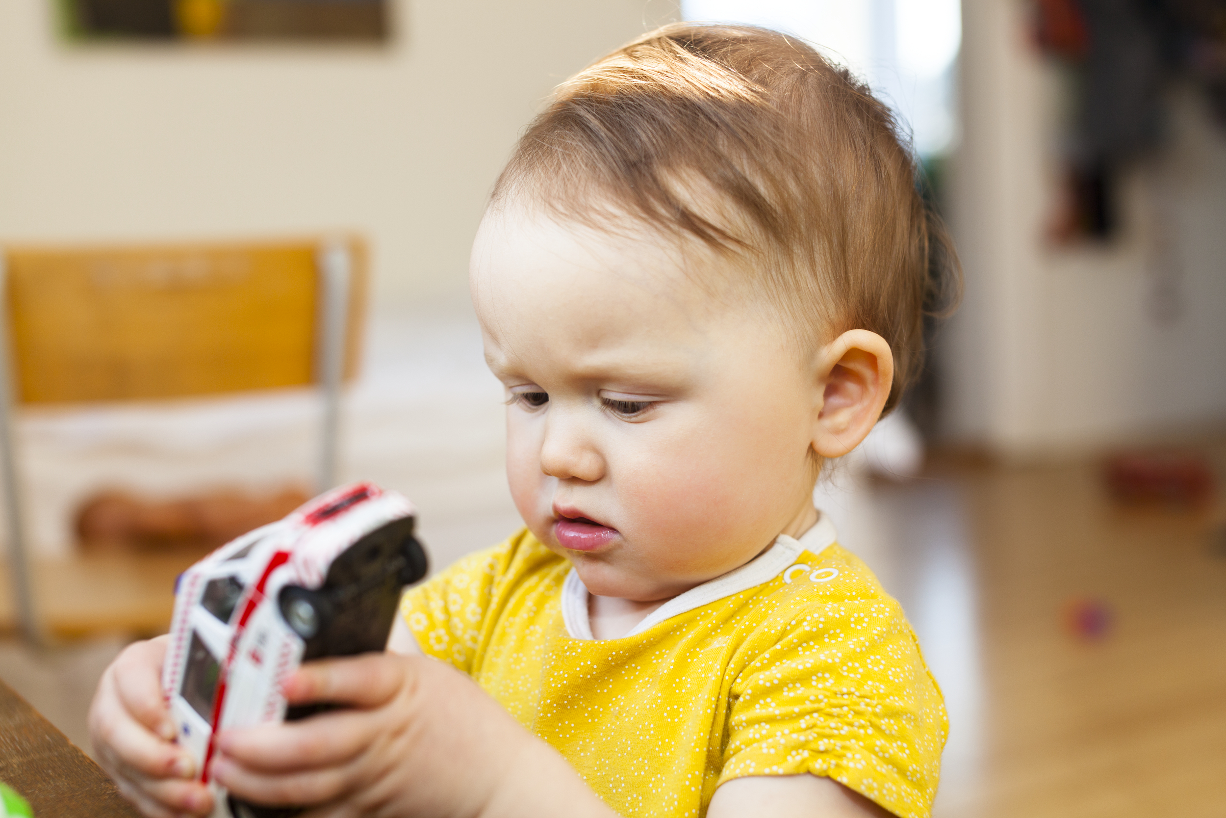 Lite barn med gul genser tetter på en lekebil.