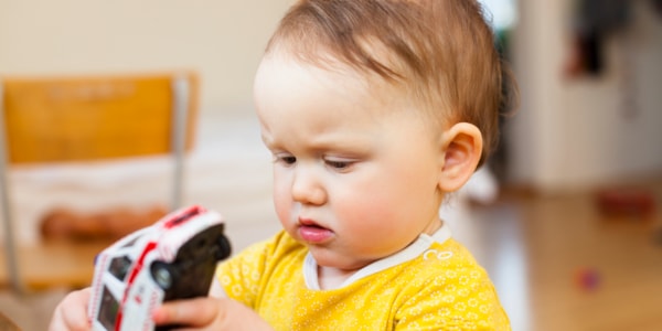 Lite barn med gul genser tetter på en lekebil.