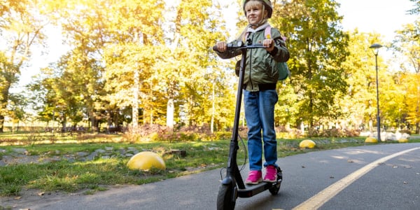 Smiling girl with helmet riding electric scooter.