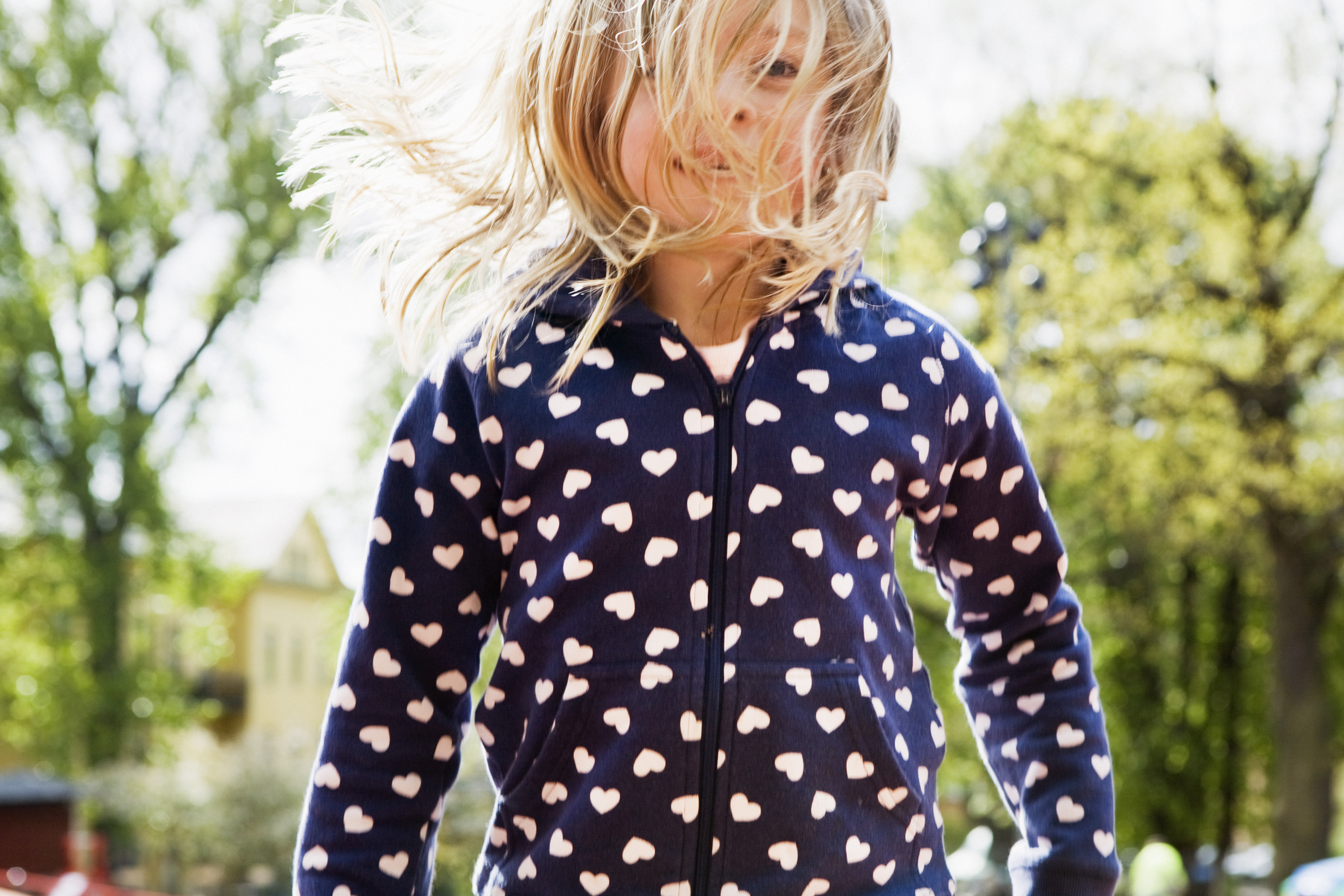 Overkroppen til en jente med lyst hår og blå hettejakke som svever over en trampoline