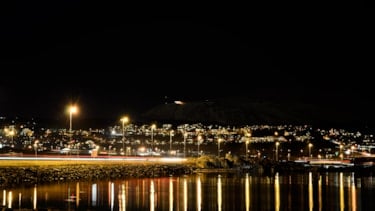Vei i mørket med gatebelysning som speiler seg i stille vann