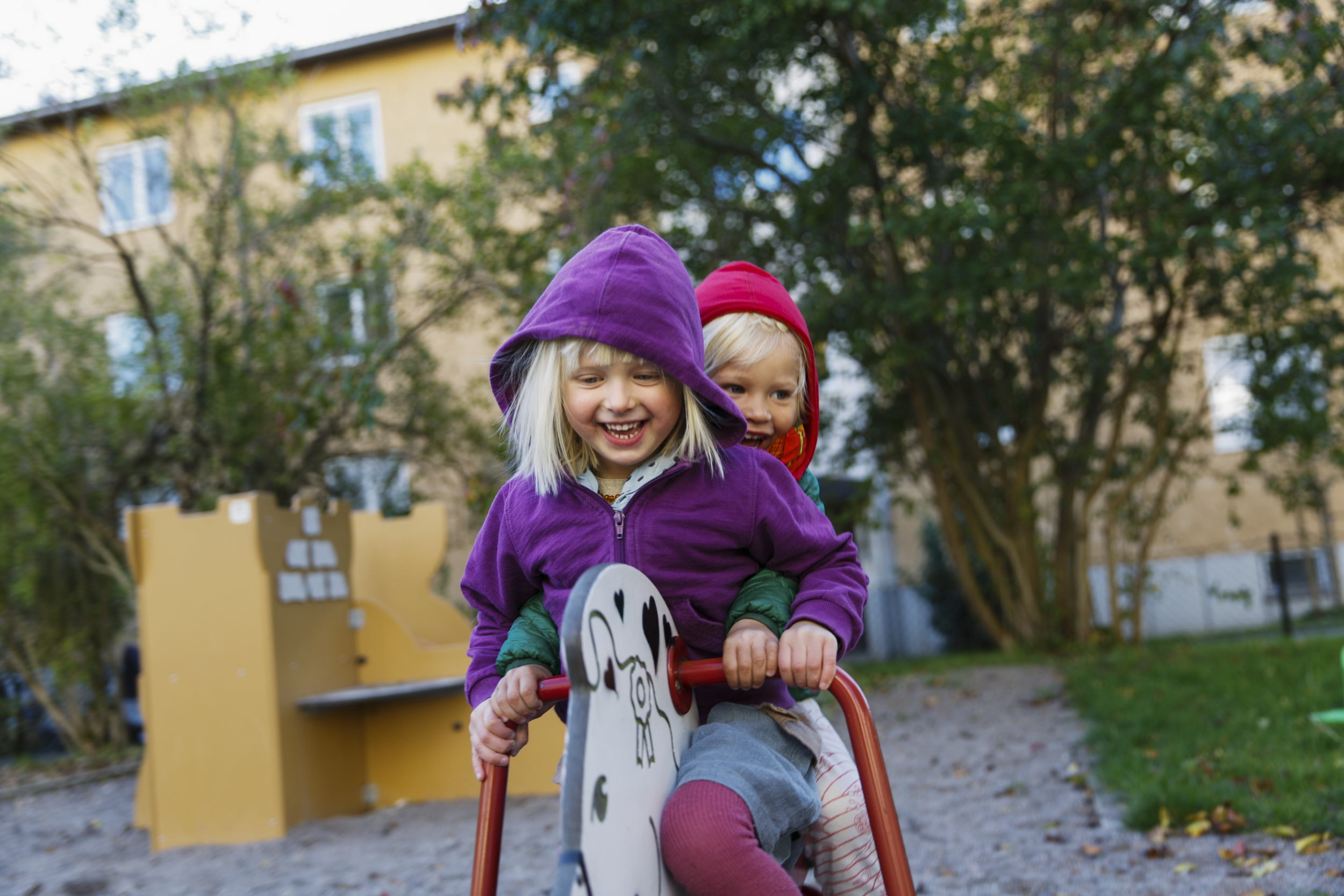 To jenter som smiler og sitter på en lekehest utendørs.
