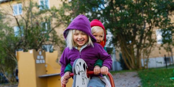 To jenter som smiler og sitter på en lekehest utendørs.