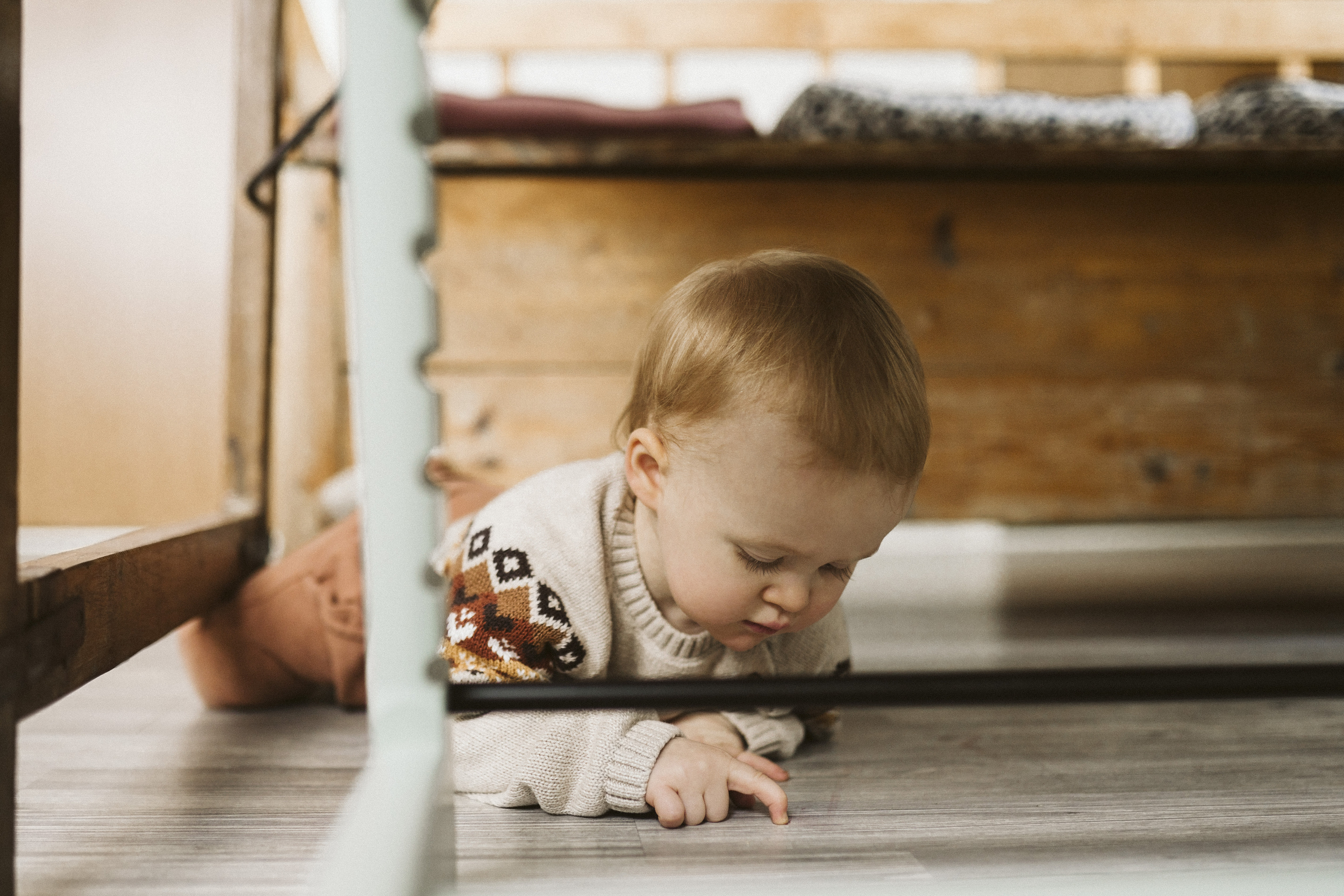 Lite barn som ligger på magen på gulvet under et bord.