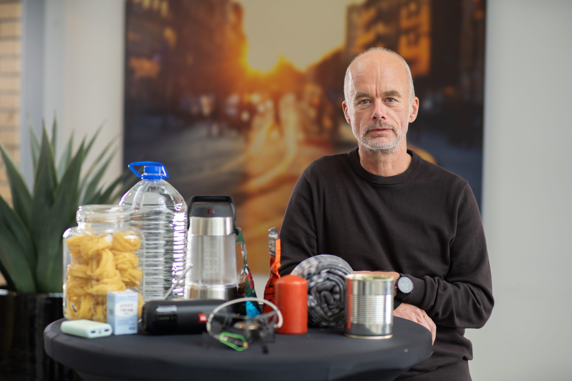 Man with gray beard beside a table with various survival items.