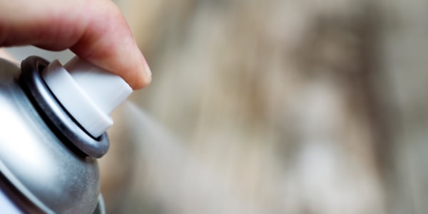 Nærbilde av en finger som trykker på en sprayboks