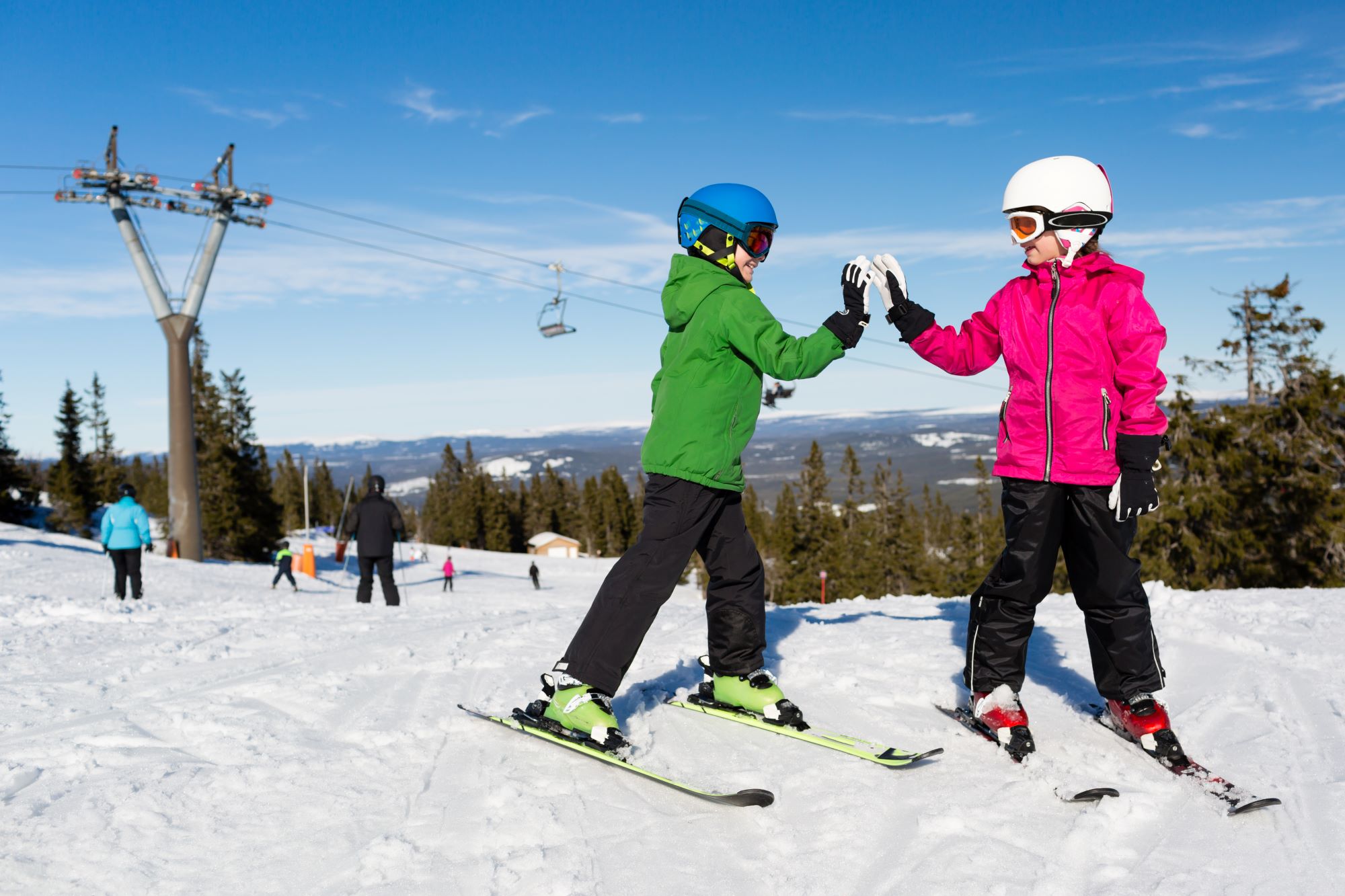 Barn med hjelm, skiklær og slalomski gir "high five" i et alpinanlegg