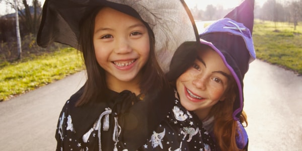 To smilande jenter utkledd i heksekostyme