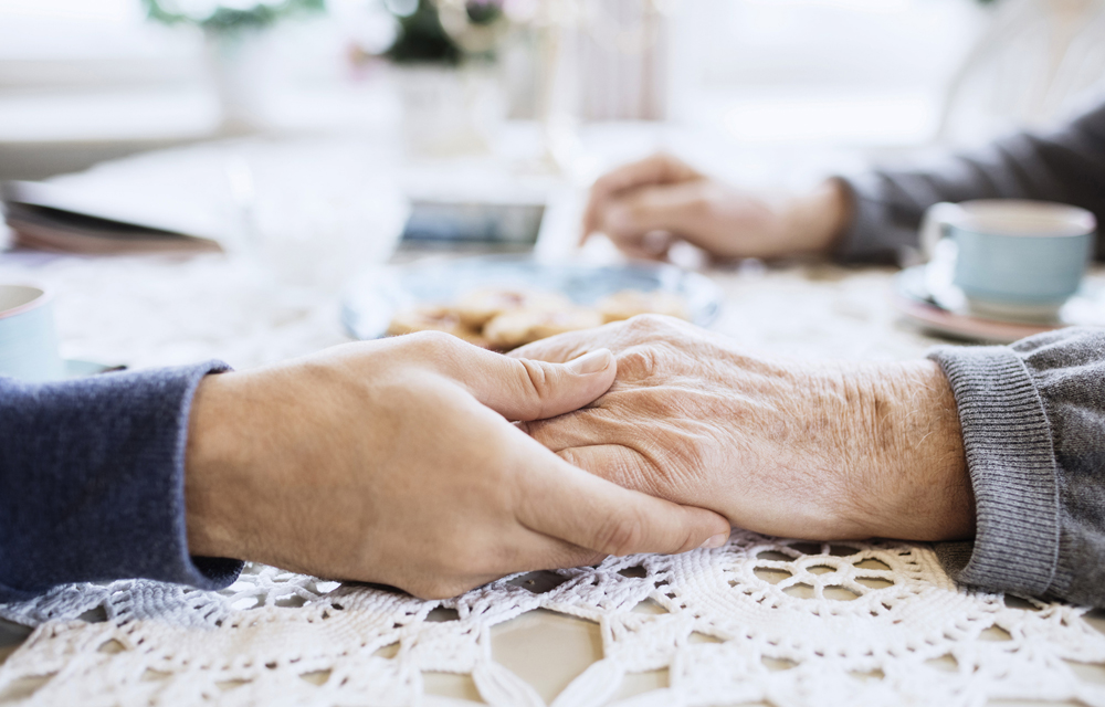 Yngre og eldre hånd som holder sammen over en heklet duk på et bord