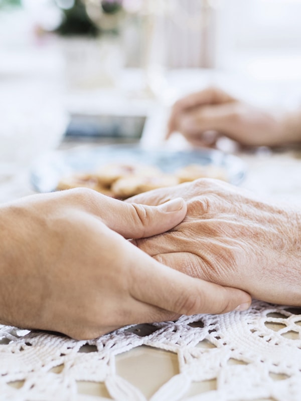 Yngre og eldre hånd som holder sammen over en heklet duk på et bord