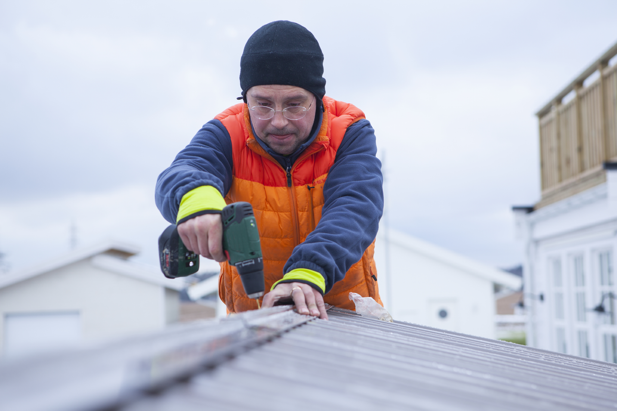 Man with hat and work clothes screws on roof tile.