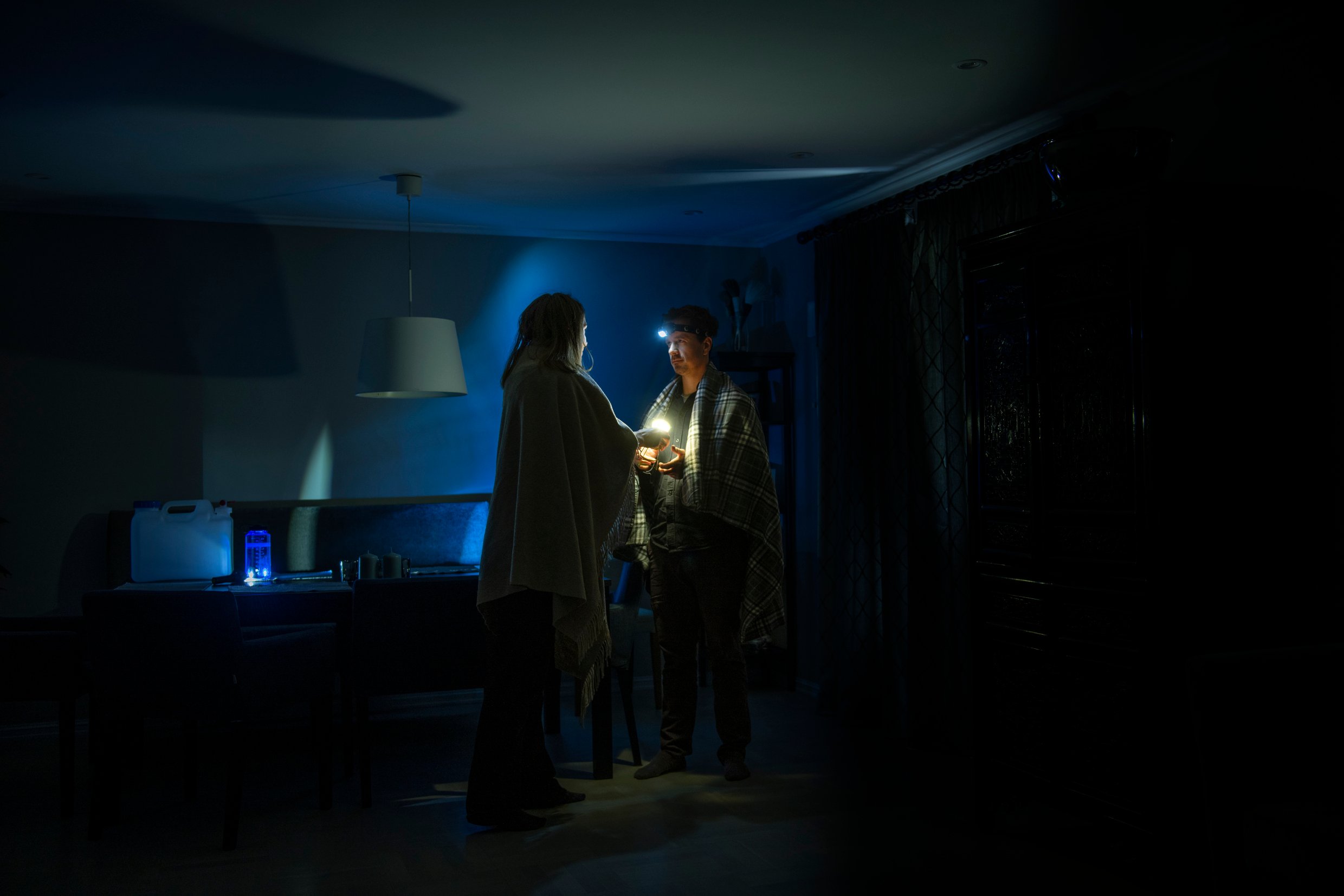A man and a woman with woollen blankets over their shoulders in a dark room.