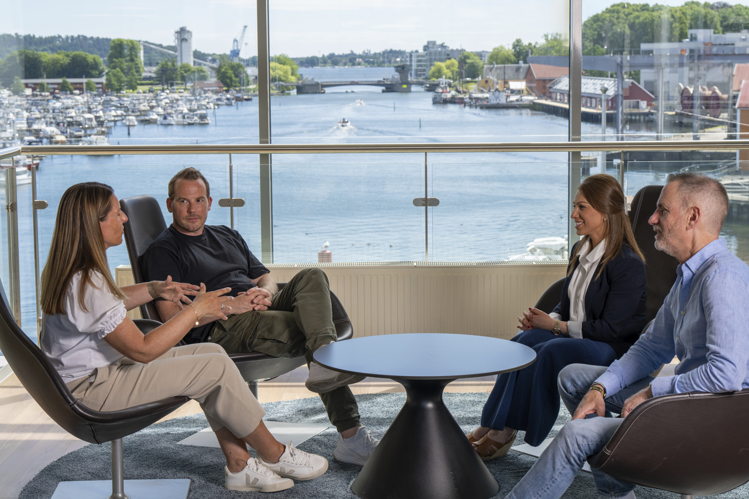 Kvinner og menn som sitter i lenestoler rundt et lavt bord og snakker sammen