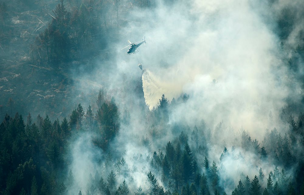 Skogbrannhelikopter i lufta over skog som brenner