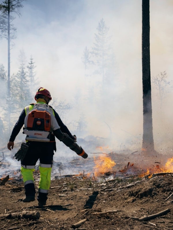 Brannmann som slokker åpne flammer i skogsterreng