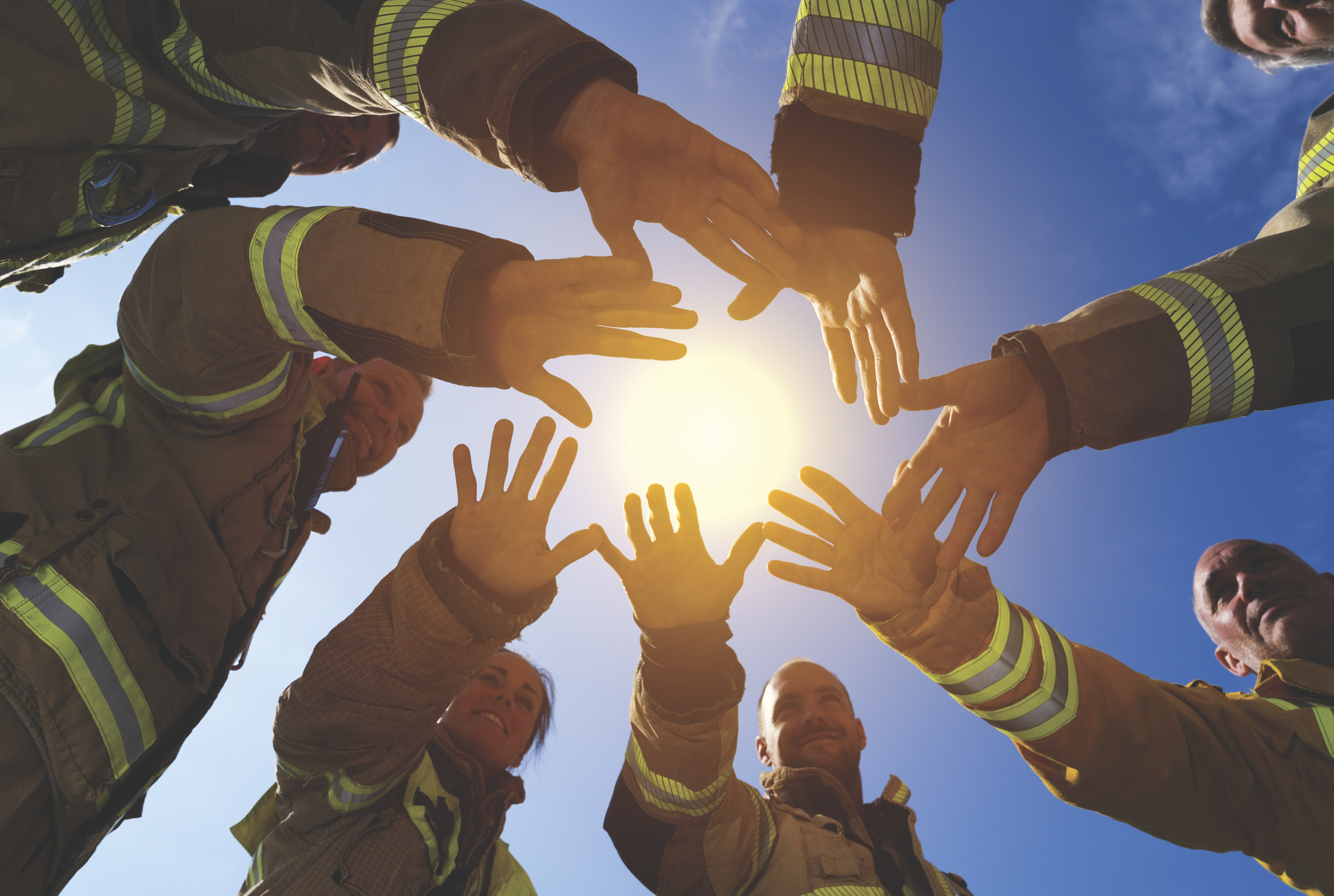Brann- og redningsmannskaper holder hendene mot hverandre. I bakgrunnen lyser en sol