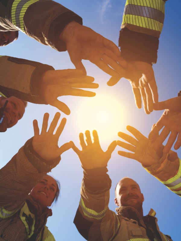 Brann- og redningsmannskaper holder hendene mot hverandre. I bakgrunnen lyser en sol