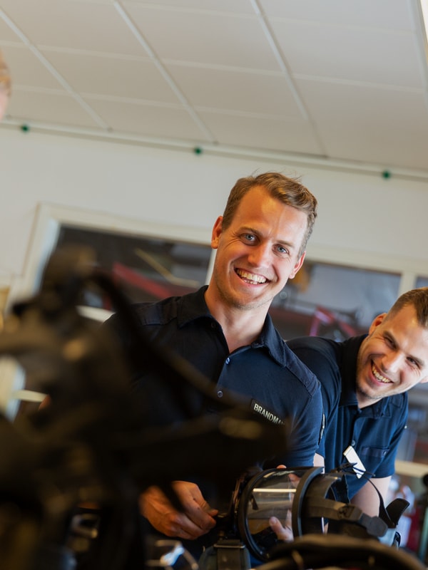 Tre glade ansatte i arbeid, kledd i uniformer, i et verkstedmiljø. De samarbeider mens de arbeider med teknisk utstyr. God atmosfære med fokus på teamarbeid og effektivitet