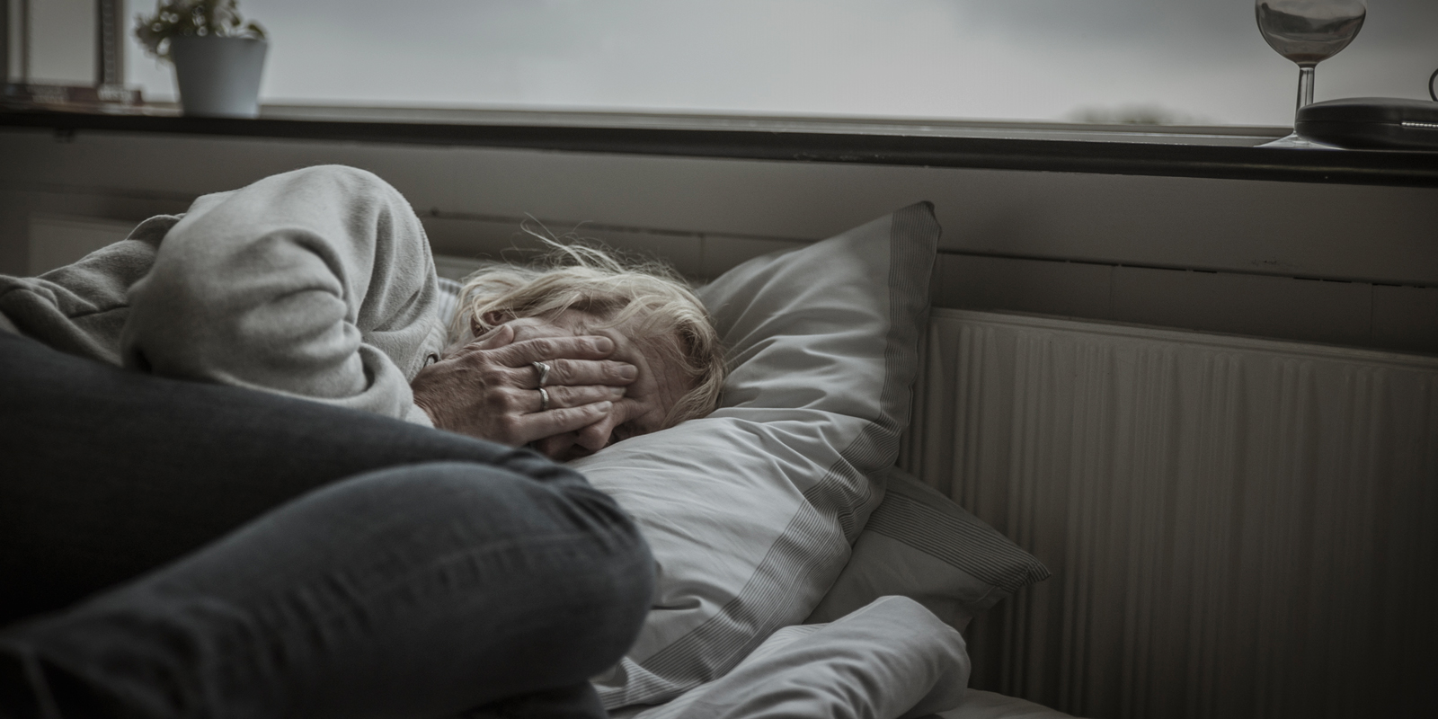 Kvinne som ligger og holder seg for ansiktet i mørkt rom