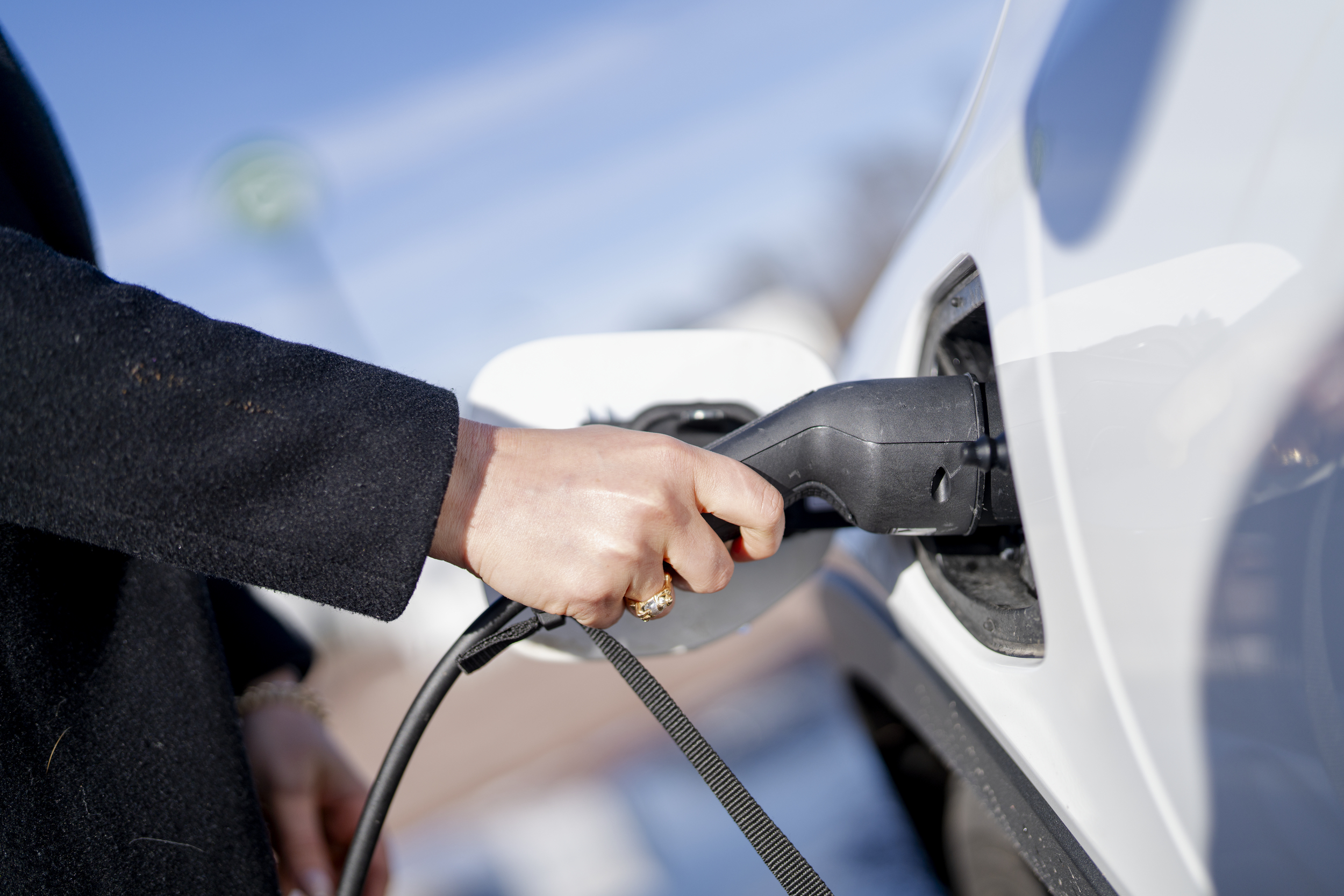 Hånd som holder en ladekabel inntil en elbil