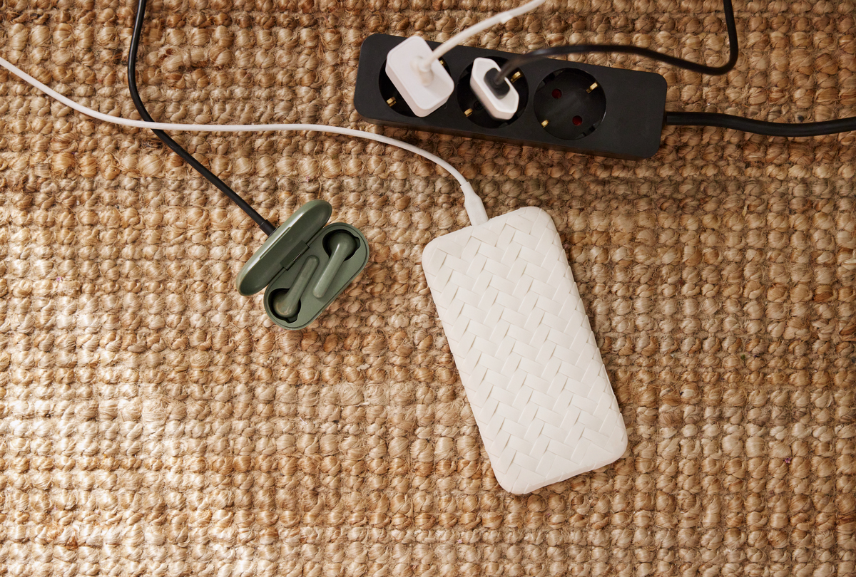 Skjøteledning med tilkoblede ladere og utstyr som ligger på et brunt teppe.