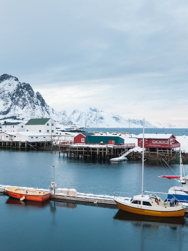 Brygge med fiskebåter foran høye snøkledte fjell nord i Norge