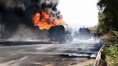 Tanbil som brenner med store flammer og svart røyk.