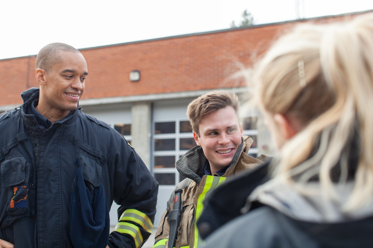 Brannmenn og en kvinne i samtale utenfor en brannstasjon