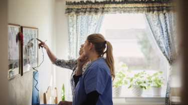 Eldre kvinne hjemme som har besøk av en kvinnelig pleier i uniform