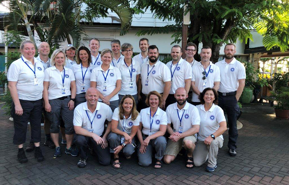 Gruppebilde av NOR EMT medlemmer oppstilt foran en bygning og grønne trær