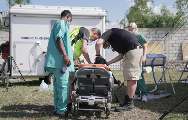 Grønnkledt helsepersonell hjelper en person på båre utendørs