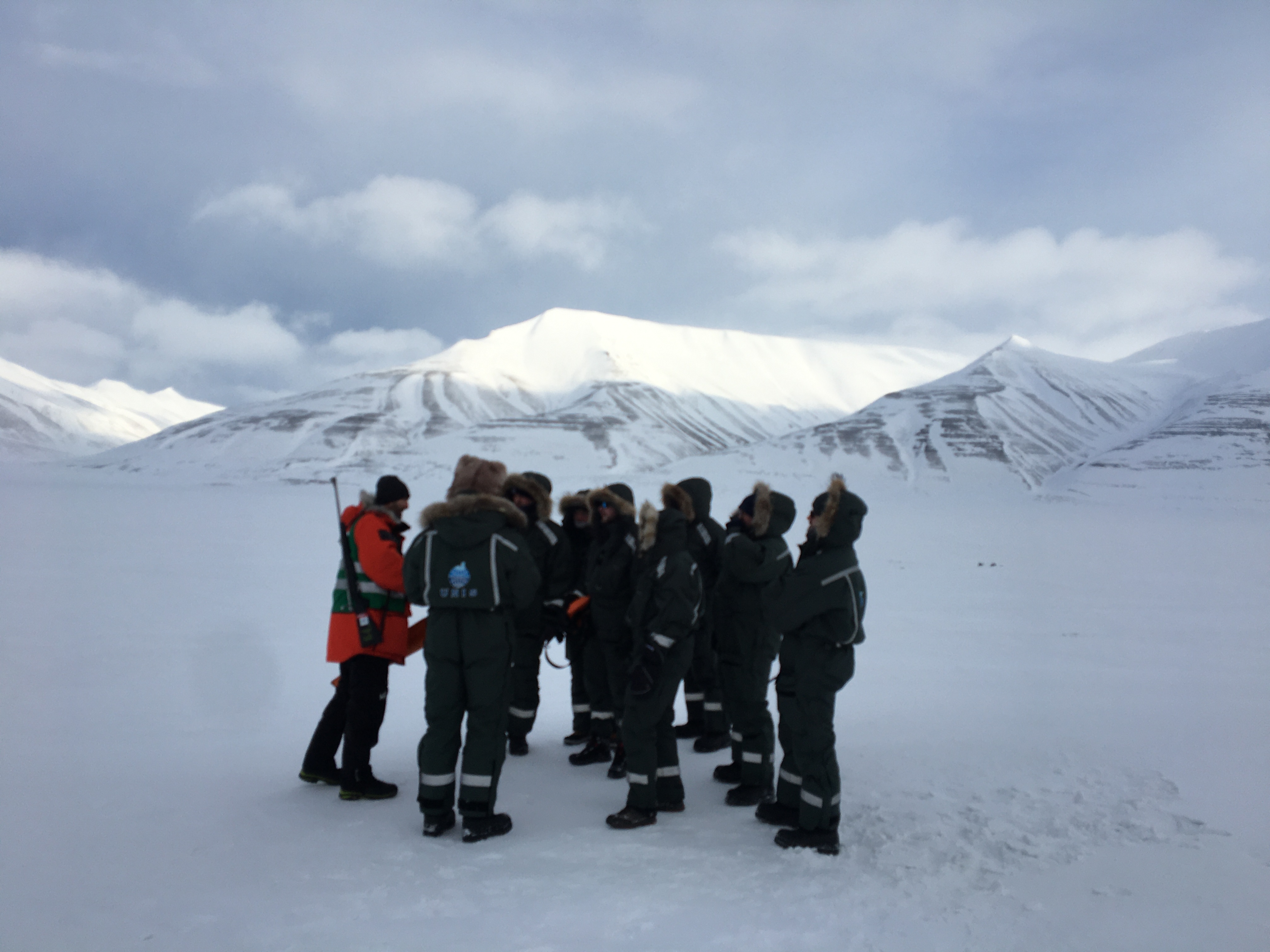 En gruppe personer i varmedresser står i snødekt landskap på Svalbard 