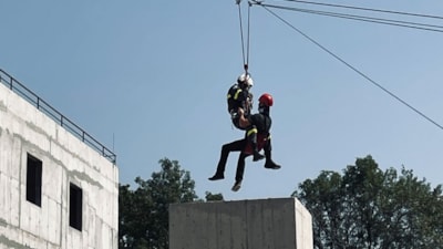 To personer som henger i klatresele fra en wire mellom bygninger