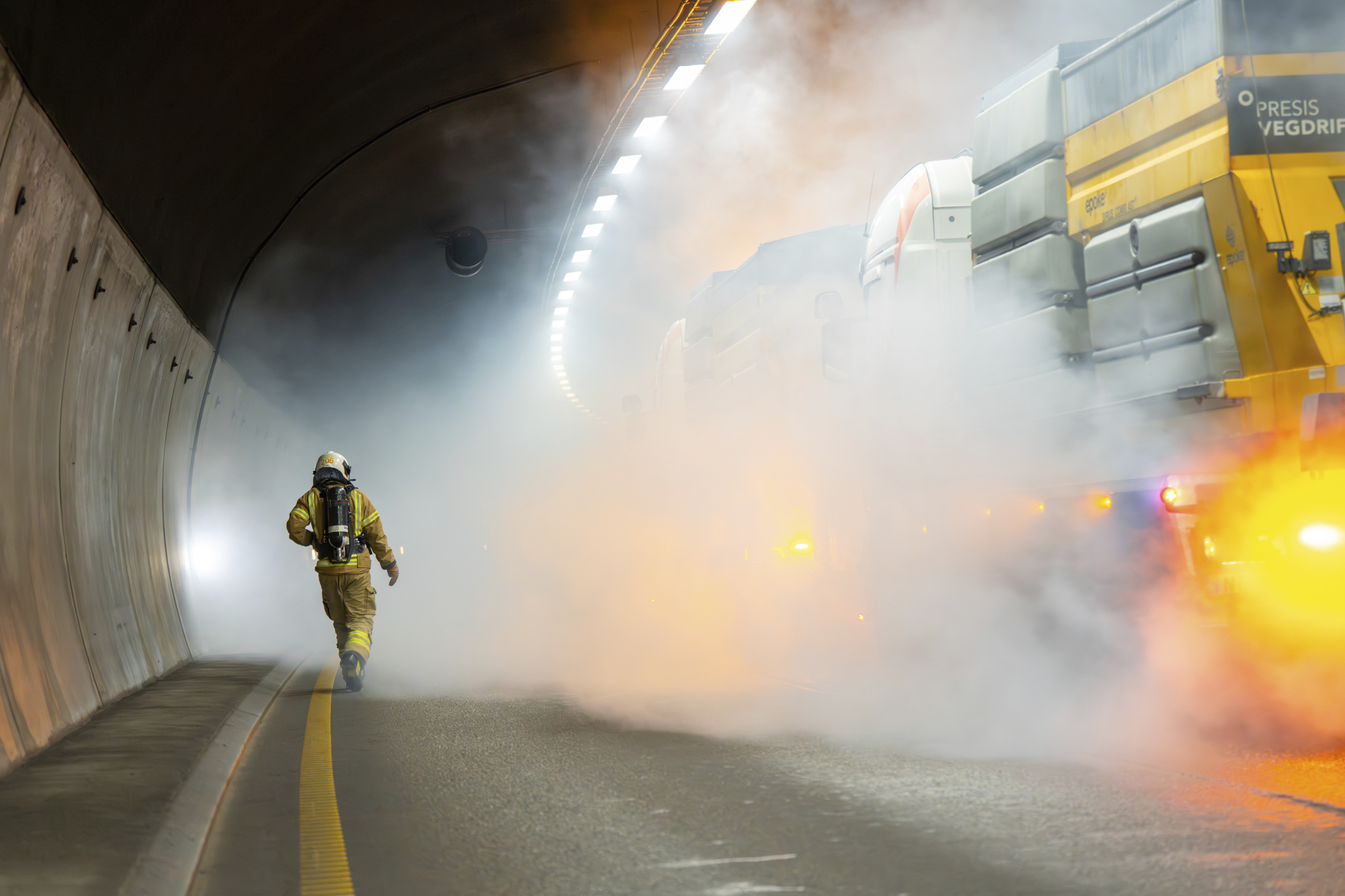 Brannmannskaper i røykfylt tunnel der det brenner i et kjøretøy