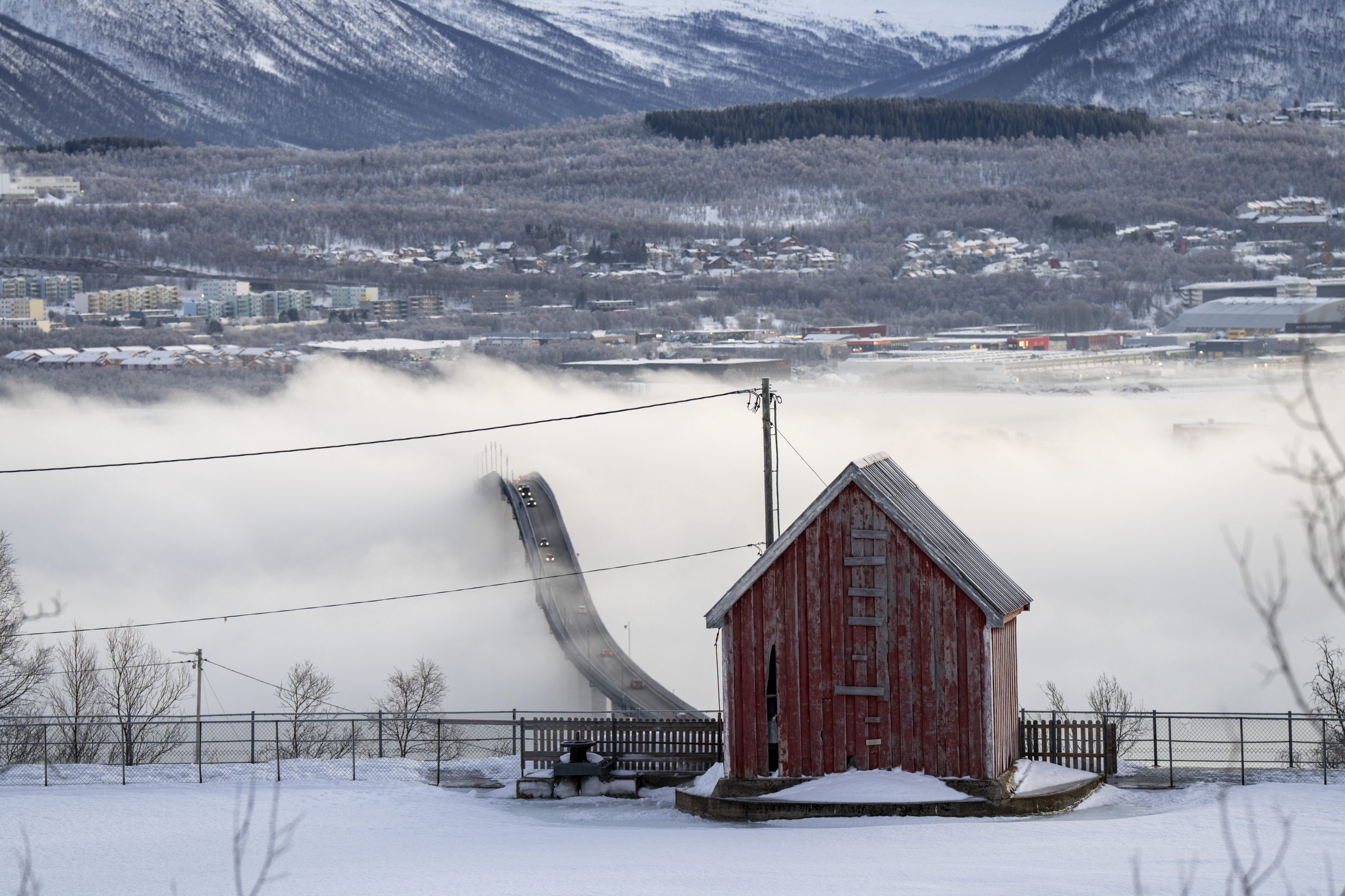 Et lite rødt hus med tåke og Tromsø by i bakgrunnen