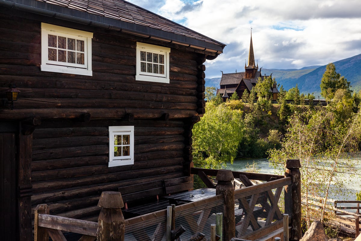 Eldre trehus med stavkirke i bakgrunnen