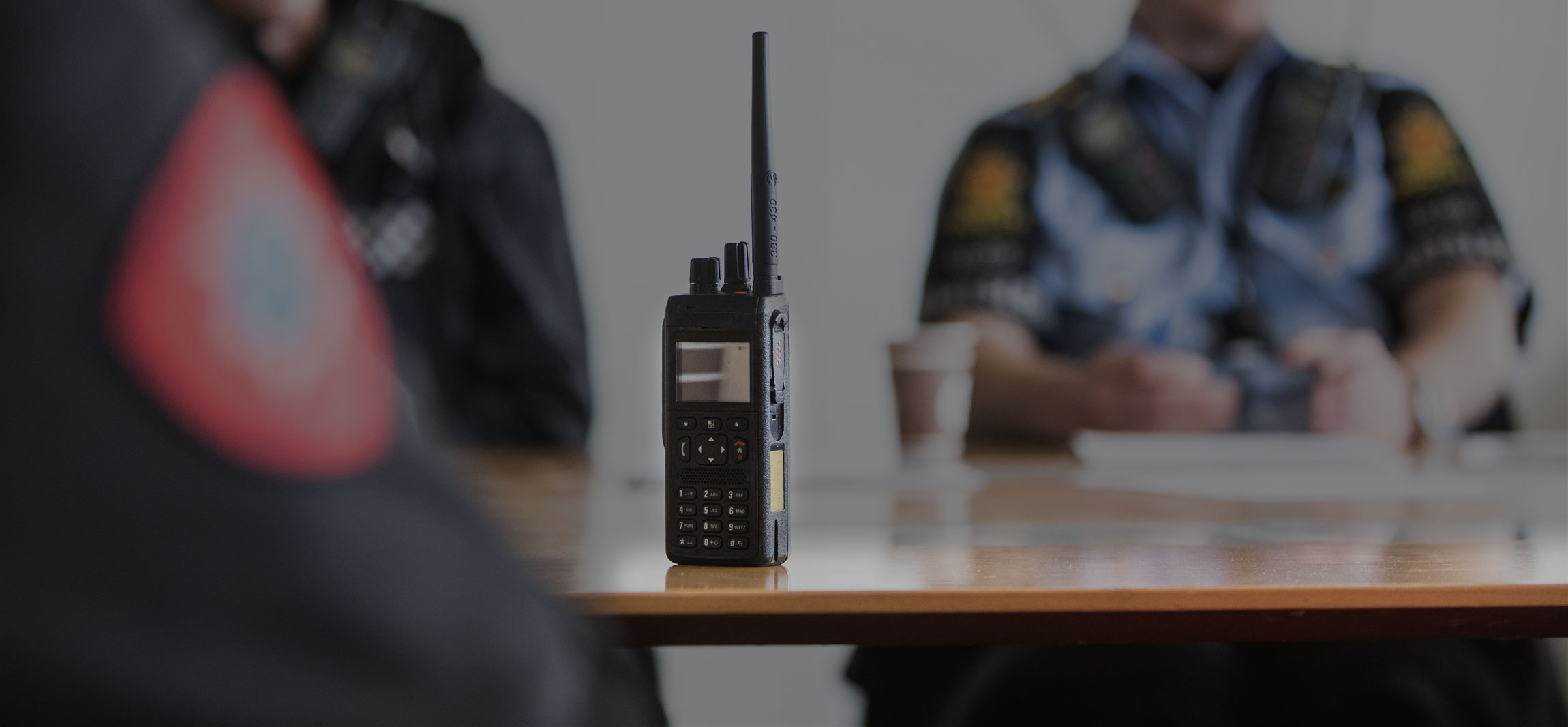 Uskarpe siluetter av personer i uniform. På et bord står en nødnett-terminal.