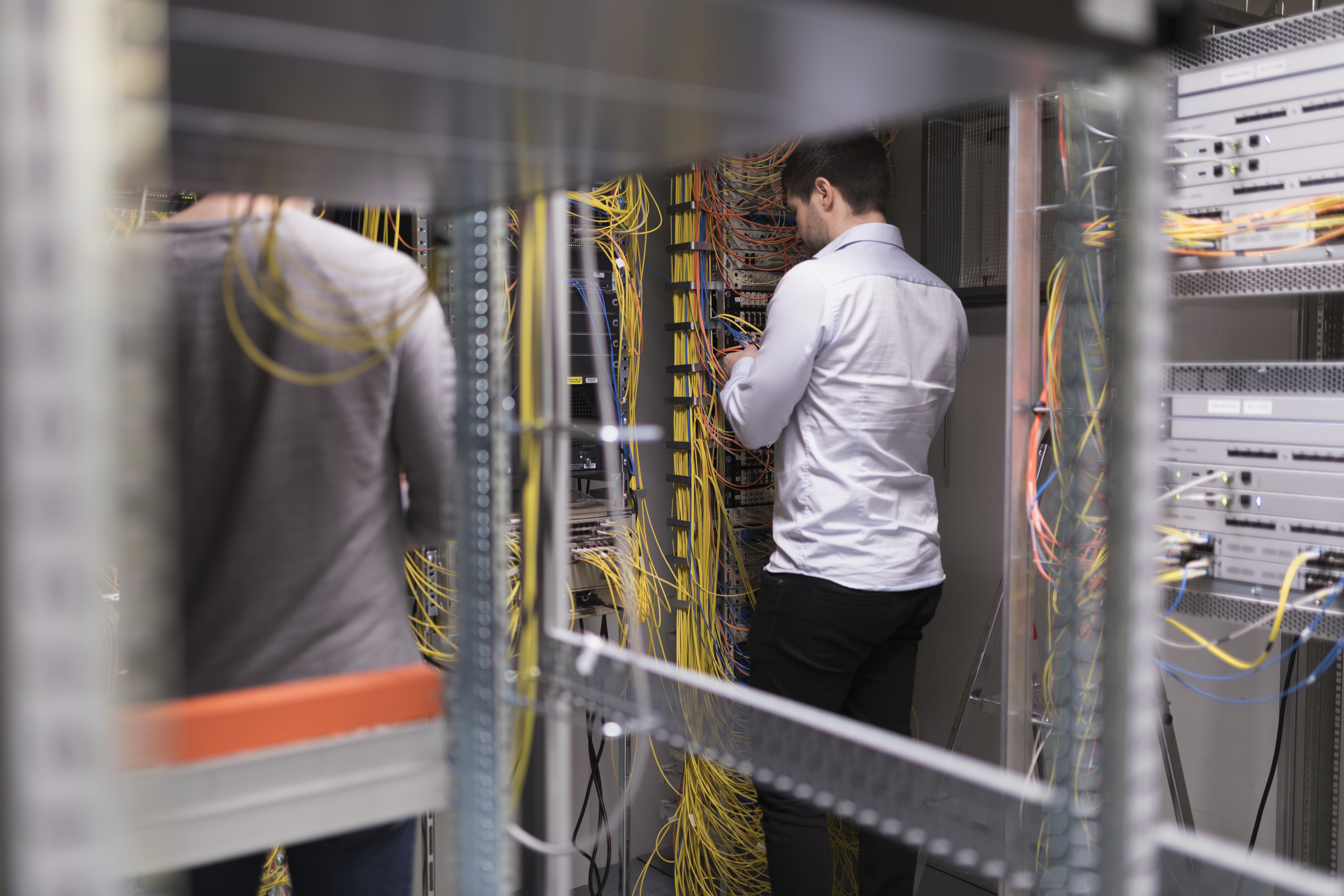 Person i skjorte og mørk bukse som holder på med ledninger i et serverrom
